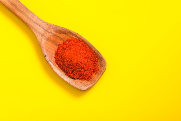 Peperoncino in polvere in un cucchiaio di legno con peperoncino rosso secco sulla superficie gialla