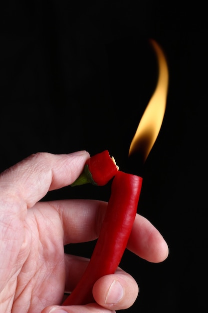 Peperoncino nelle mani di un accendino con una fiamma ardente