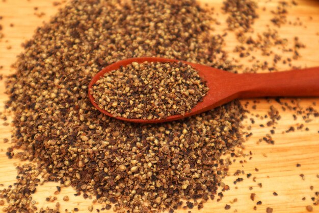 Peperoncino nero schiacciato Piper nigrum L in un cucchiaio di legno e alcuni sparsi visti dall'alto