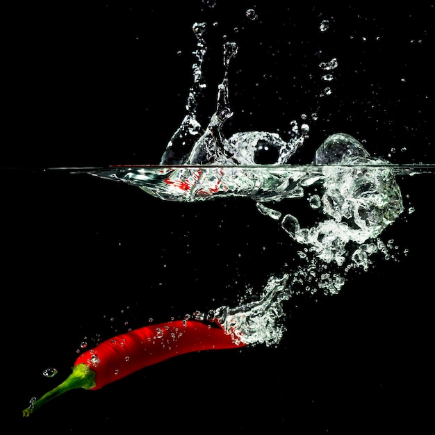 Peperoncino rosso rosso che spruzza nell&#39;acqua contro fondo nero