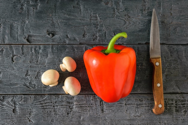 Peperone dolce rosso maturo con funghi e coltello su un tavolo di legno