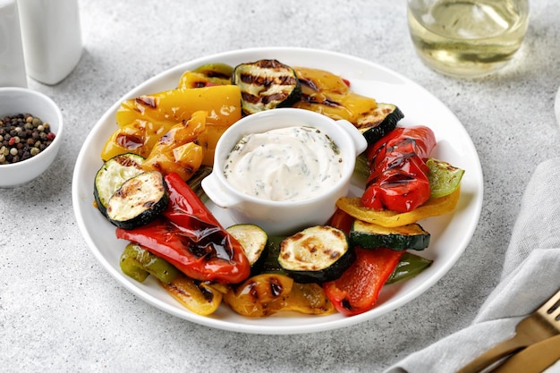 Peperoni e zucchine grigliate di verdure su un piatto bianco e sfondo grigio Cibo vegano