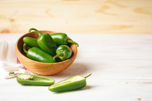 Peperoni jalapeno verdi in un piatto di legno su uno sfondo di legno, spazio per il testo.