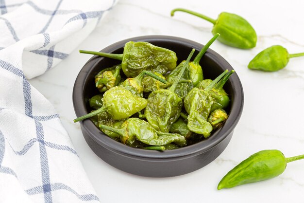 Peperoni Padron cotti in una ciotola sul tavolo di marmo. Antipasto spagnolo tradizionale