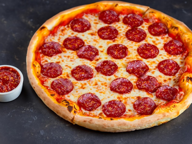 Peperoni per pizza italiana tradizionale con salame e formaggio su un metallo di pietra ardesia scuro o cemento