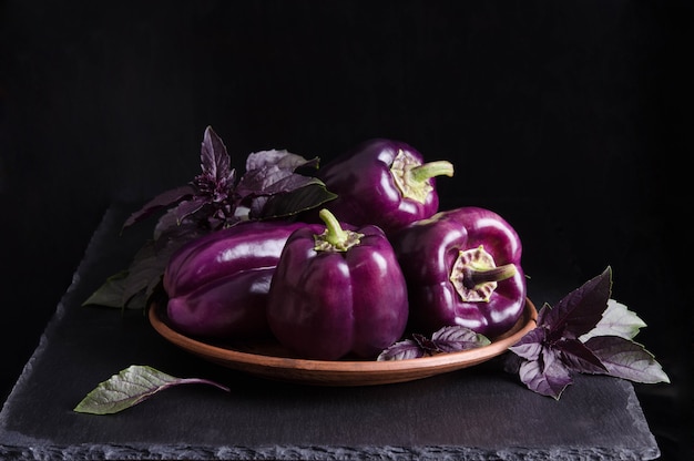 Peperoni viola scuro nel piatto con foglie di basilico