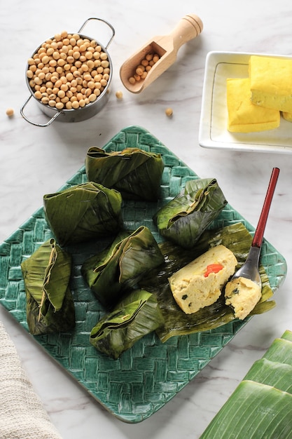 Pepes Tahu è il tofu speziato indonesiano avvolto con foglie di banana e cotto a vapore, cibo tipicamente indonesiano di Giava occidentale (sudanese). Tofu al vapore con basilico asiatico, sfondo bianco