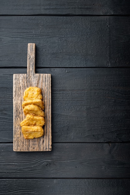 Pepite di petto di pollo fritte sulla tavola di legno nera, vista dall'alto.