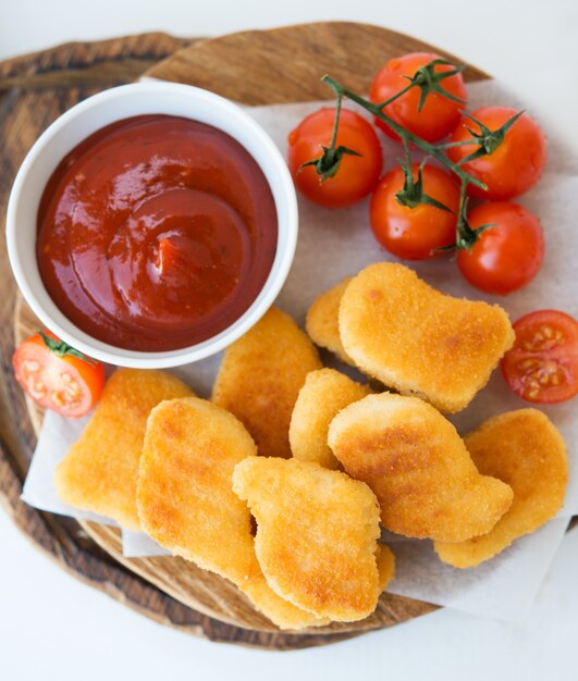 Pepite di pollo fatte in casa con salsa e pomodori su una tavola di legno, vista dall'alto