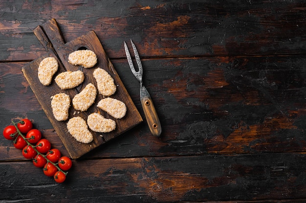 Pepite di pollo non cotte impostate su vecchio tavolo in legno scuro sfondo vista dall'alto piatto con copia spazio per il testo