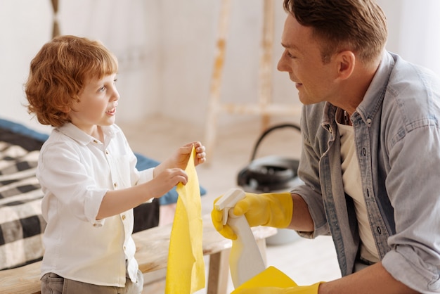 È per te. Piccolo figlio in piedi in posizione semi e tenendo lo spolverino con entrambe le mani mentre guarda negli occhi di suo padre