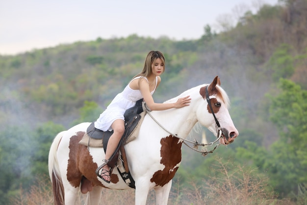 Per tutta la lunghezza della donna sul vestito a cavallo sul campo da alberi contro il cielo