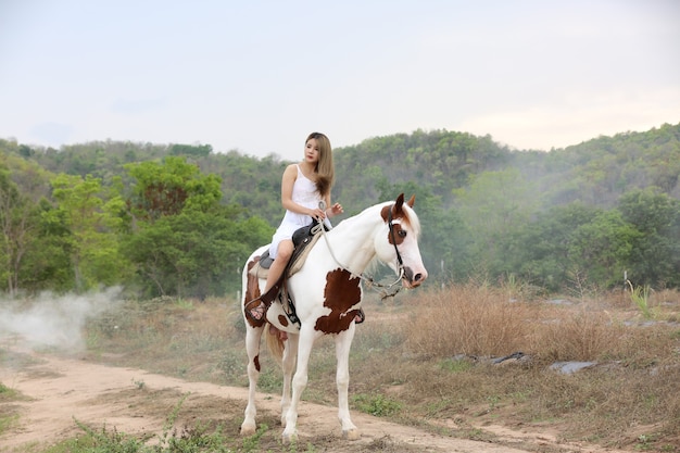 Per tutta la lunghezza della donna sul vestito a cavallo sul campo da alberi contro il cielo