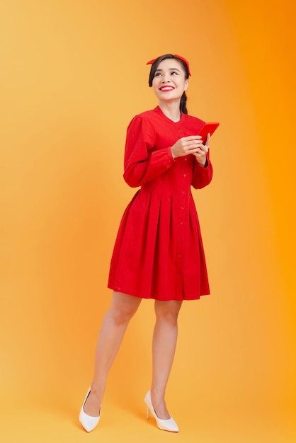 Per tutta la lunghezza della giovane donna asiatica che usa il telefono quando è in piedi isolato su sfondo arancione colorato