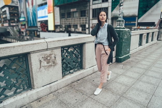 per tutta la lunghezza della giovane signora asiatica dell'ufficio che cammina sul cavalcavia indossando un abito casual intelligente che va al lavoro al mattino. elegante donna giapponese sul ponte dotonbori nipponbashi all'aperto guardando da parte rilassarsi