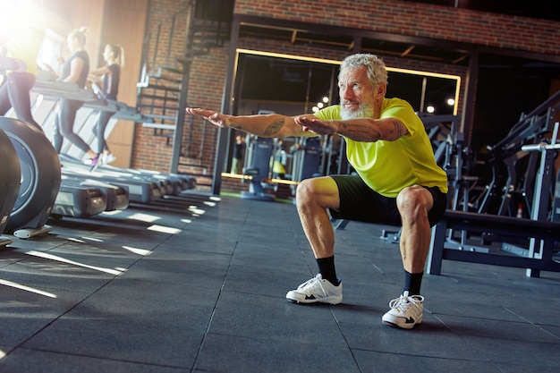 Per tutta la lunghezza di un uomo caucasico maturo in abbigliamento sportivo che si allena in palestra facendo squat