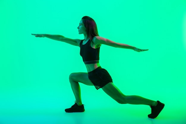 Per tutta la lunghezza di una bellissima giovane ragazza fitness che si allena isolata sul muro verde, facendo affondi