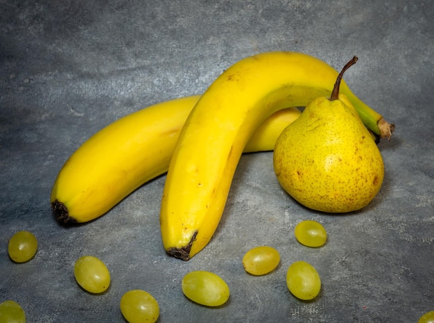 Pera due banane e una manciata di uva verde su sfondo nero