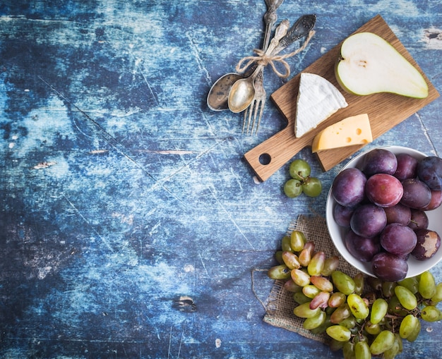 Pera matura fresca, vassoio di formaggi assortiti, uva, prugne in una ciotola