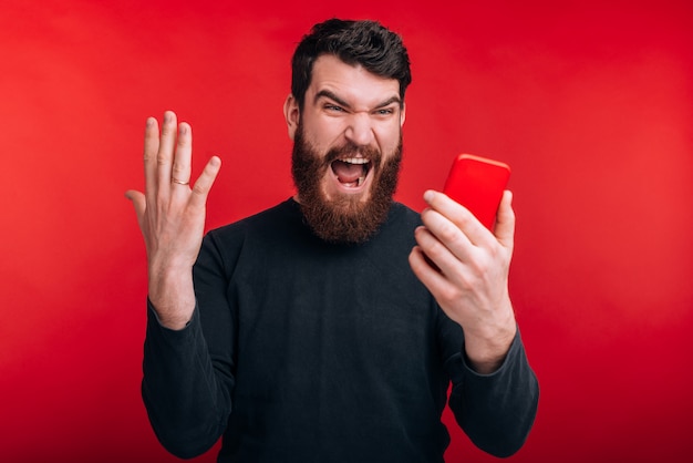 Perché non funziona ?! L'uomo barbuto arrabbiato sta gridando a questo telefono sulla parete rossa