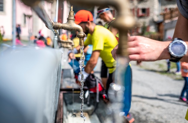 Perdita d&#39;acqua da un rubinetto e da corridori che riempiono lo zaino in una corsa di montagna