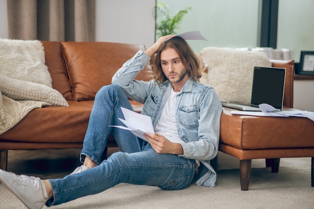 Perdita di lavoro. Giovane uomo in camicia di jeans che tiene documenti e che sembra stressato