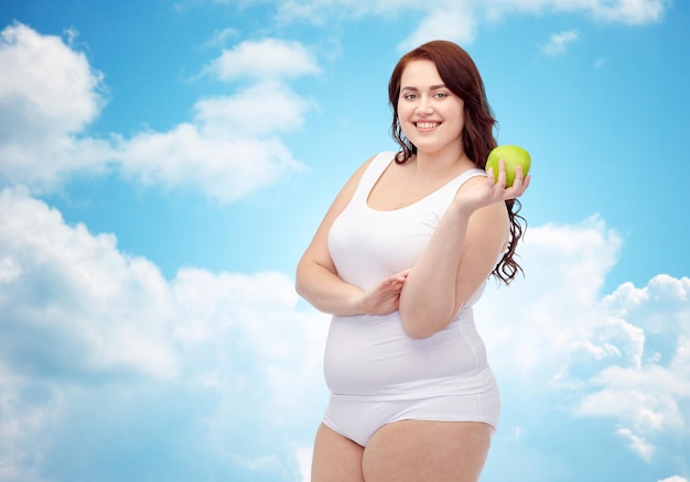 perdita di peso, dieta, dimagrimento, alimentazione sana e concetto di persone - giovane donna felice plus size in biancheria intima con mela verde su sfondo blu cielo e nuvole