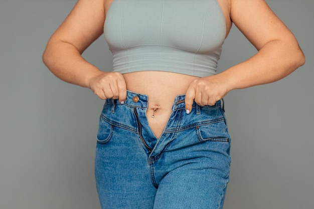 perdita di peso e problema di sovrappeso una donna grassa in una canotta e jeans sta cercando di abbottonare o pu