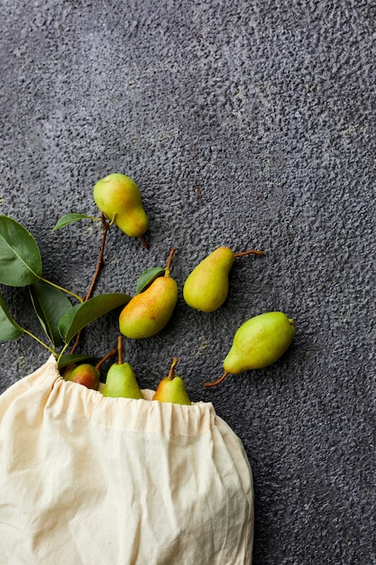 Pere fresche di frutta matura in una borsa ecologica riutilizzabile per la spesa su uno sfondo scuro, concetto di drogheria, piatto, ecologico, raccolto autunnale. Copia spazio.