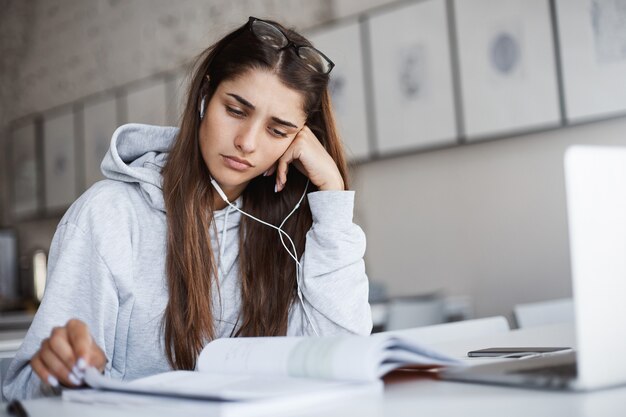 Perfetta giovane studentessa sconvolta che non capisce l'argomento di un libro che ascolta un corso educativo online.