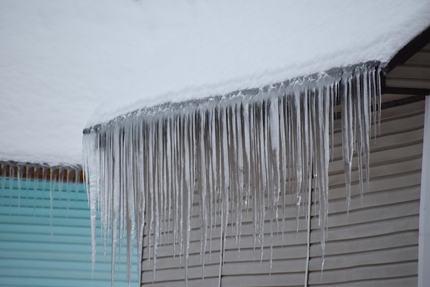 Pericolo di grossi ghiaccioli che cadono sulla testa delle persone. il ghiaccio pende dal tetto in inverno. ghiaccioli sul tetto della casa