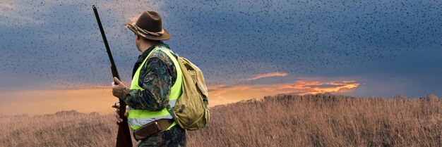 Periodo di caccia aperto stagione autunnale Un cacciatore con una pistola in mano in abiti da caccia nella foresta autunnale in cerca di un trofeo Un uomo in piedi con armi e cani da caccia che rintraccia la selvaggina