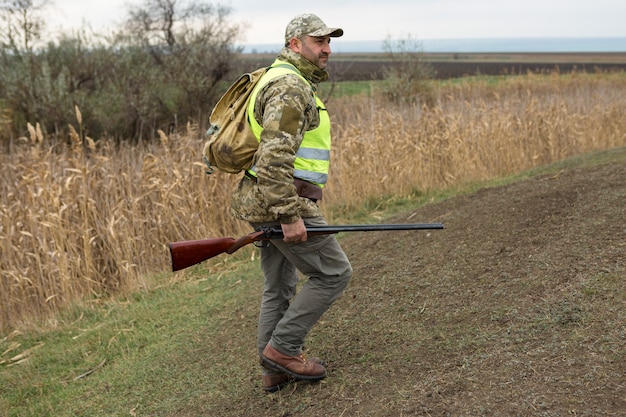 Periodo di caccia, stagione autunnale aperta. Un cacciatore con una pistola in mano in abiti da caccia nella foresta di autunno in cerca di un trofeo.