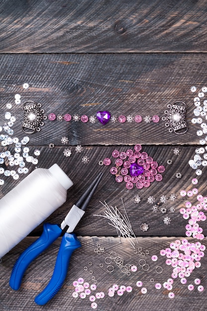 Perline, ciondoli, pinze, cuori di vetro e accessori per creare gioielli fatti a mano su tavola di legno, realizzando bracciali