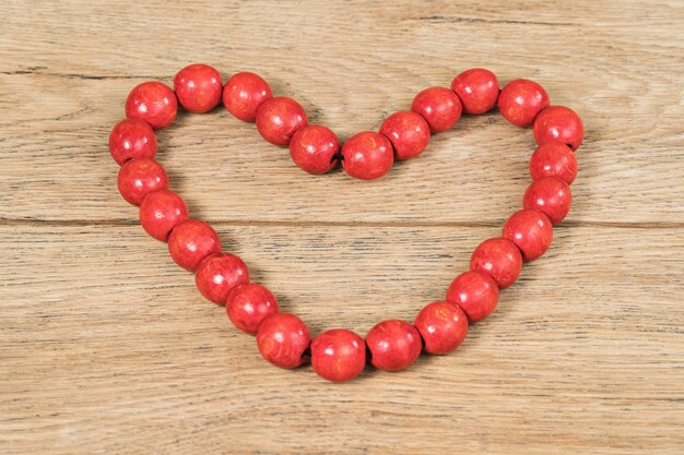 Perline di legno rosse disposte a forma di cuore su un vecchio tavolo di legno