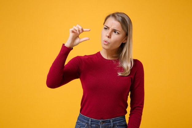 Perplesso giovane donna bionda ragazza in abiti casual in posa isolato su sfondo giallo arancione in studio. Concetto di stile di vita delle persone. Simula lo spazio della copia. Gesticolando dimostrando le dimensioni con l'area di lavoro.