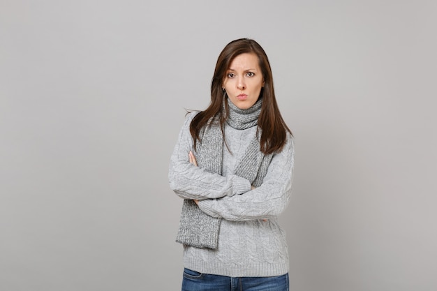 Perplesso interessato giovane donna in maglione grigio, sciarpa tenere le mani piegate isolate su sfondo grigio muro. Stile di vita sano, persone sincere emozioni, concetto di stagione fredda. Mock up copia spazio.