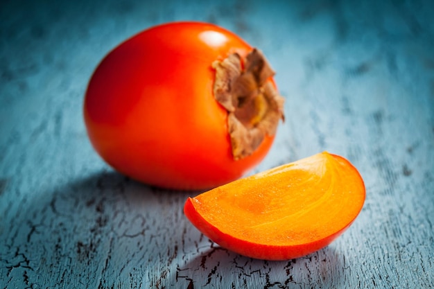 Persimmon fresco maturo con fetta su uno sfondo di legno blu