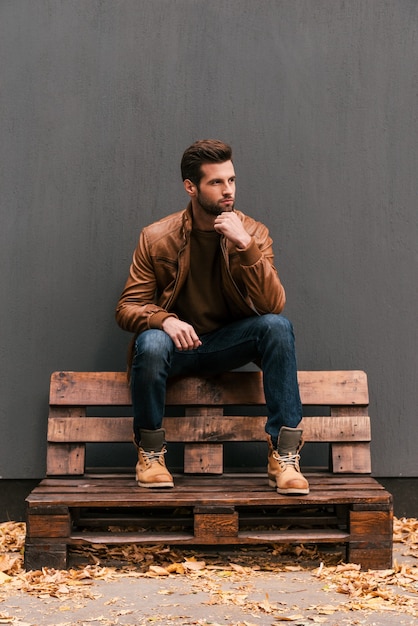 Perso nei pensieri. Giovane premuroso seduto sul pallet di legno e guardando lontano