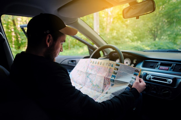 Perso nel giovane autista della foresta che si siede in macchina mentre tenendo mappa e guardando da parte