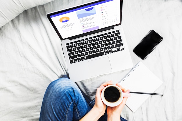 Persona a letto con tazza di caffè e laptop