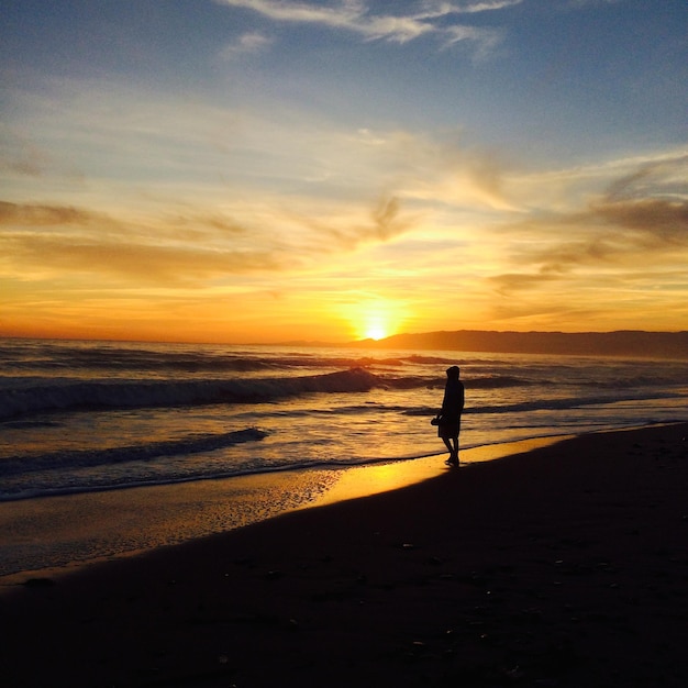 Persona a silhouette in piedi sulla spiaggia contro il cielo arancione durante il tramonto
