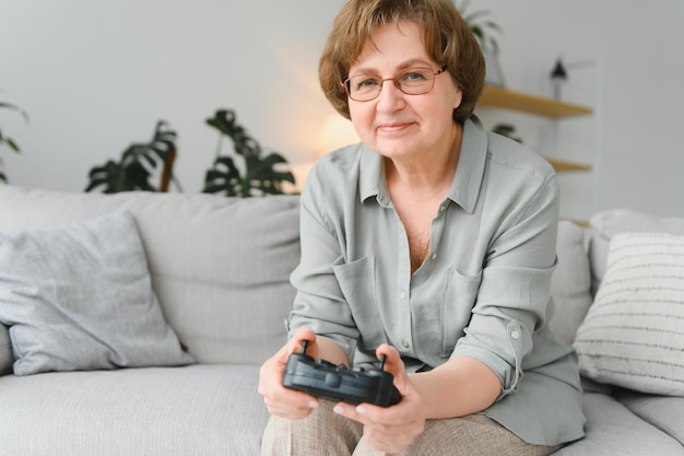 Persona anziana che si diverte a giocare su una console con un videogioco seduto sul divano