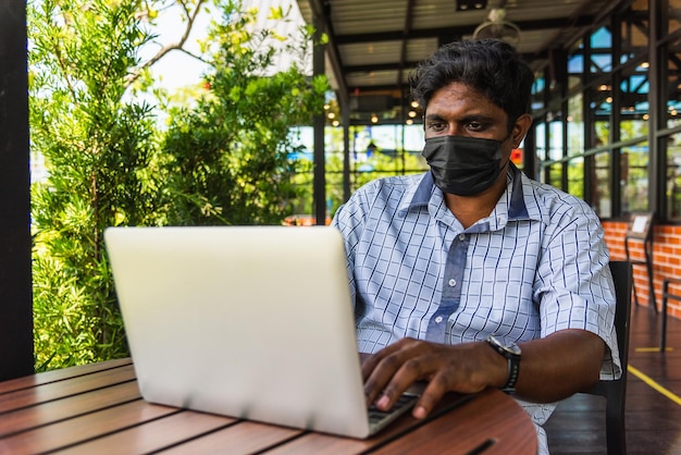 Persona asiatica felice dell'uomo di colore della mano che si siede lavorando con il computer portatile, la tecnologia del dispositivo e la connessione in rete online al bar caffetteria