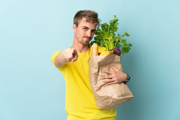 Persona bionda prendendo un sacchetto di cibo da asporto isolato su sfondo blu rivolto verso la parte anteriore con felice espressione