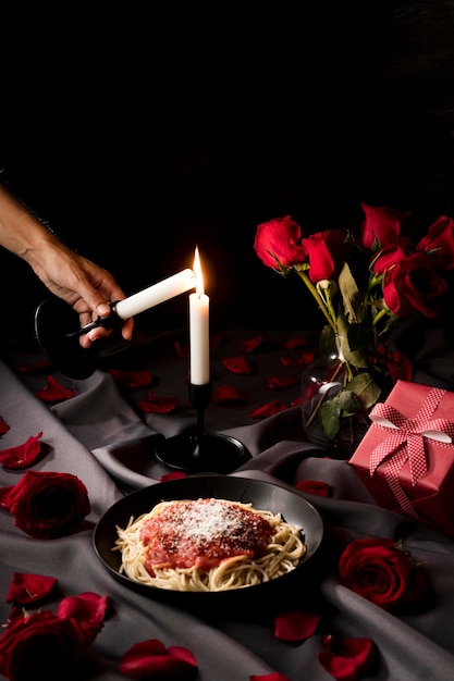 Persona che accende una candela per la cena di San Valentino con pasta e rose