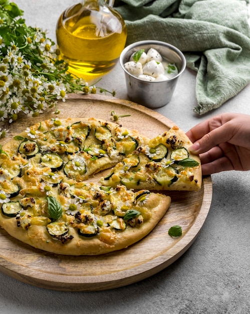 Persona che afferra una fetta di pizza con fiori di camomilla