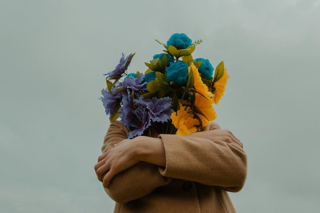 Persona che copre la faccia con un bouquet contro un cielo limpido