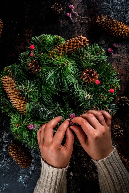 Persona che decora la corona verde di Natale con pigne e bacche rosse invernali