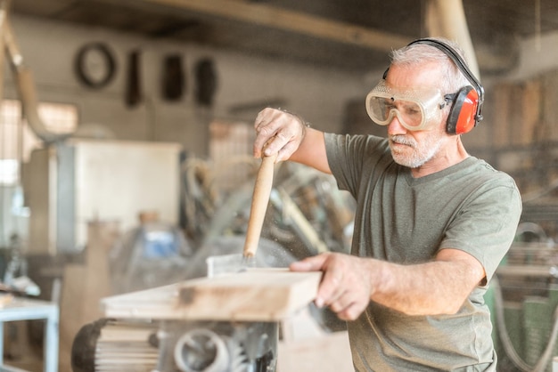 Persona che lavora con una tavola di legno in equipaggiamento di sicurezza, sfondo sfocato orizzontale